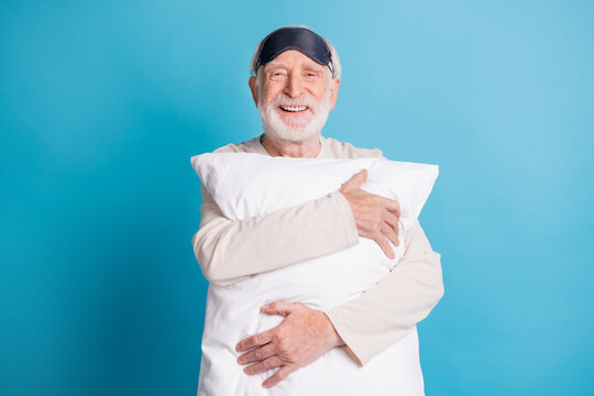 Photo portrait of positive old man in eye mask hugging pillow isolated on pastel blue colored background