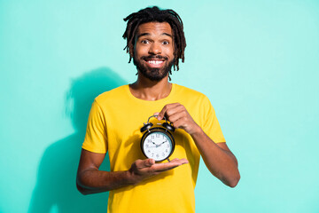 Photo of young happy smiling cheerful handsome african man wear yellow t-shirt hold clock isolated on teal color background