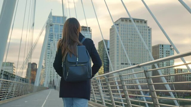 A girl tourist with backpack walking on Millennium Bridge, London in lockdown. A female in a coat during winter with no people walking in front of most famous London landmarks in slow-motion in 4K.