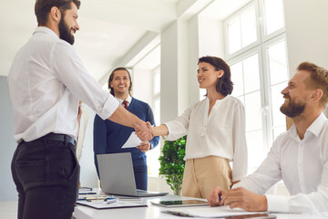 Confident young business team meets its client and shakes hands in a bright and modern office.