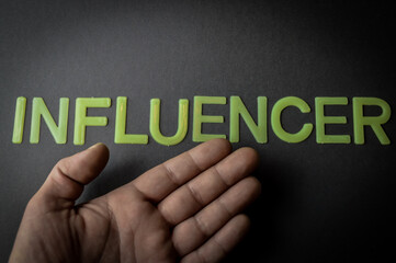 Human hand showing the word Influencer written with plastic letters on dark gray paper background, concept
