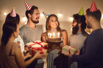 Happy young woman holding her birthday cake and thanking friends for party and presents