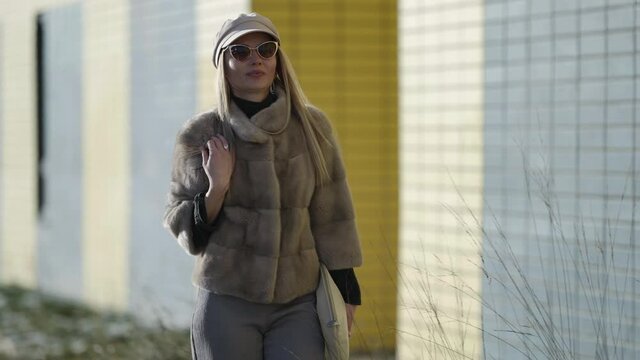 blonde woman is wearing expensive fur jacket and sunglasses is strolling alone in downtown