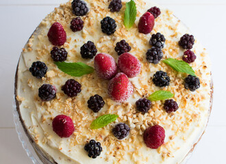 A delicious cake with whipped cream, blackberries and strawberries on top of the cocoa cake.