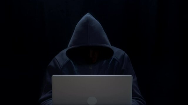 The hacker uses a laptop. A hooded man with an invisible face in a dark room. Cyber attack.