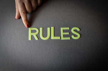 Human finger pointing the word Rules written with plastic letters on dark gray paper background,...