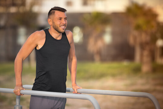 Sporty young man doing triceps dips on parallel bars outdoors. Doing exercises on parallel bars in the park