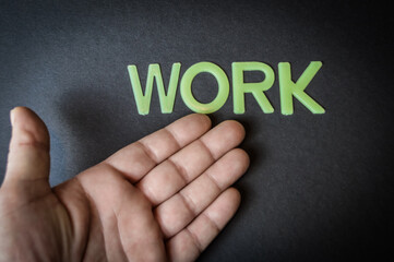Human hand showing the word Work written with plastic letters on dark gray paper background, concept	