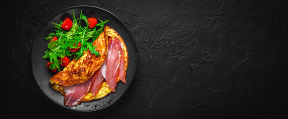 omelette with prosciutto and salad on black plate on Dark grey black slate background