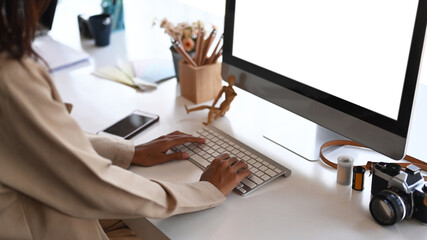 Young female photographer hands typing on keyboard while sitting in front of computer at creative workspace.