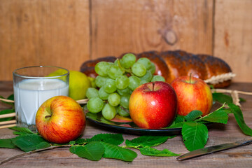 lemon, apples, green grapes, wheat and a glass with milk on a wooden table.