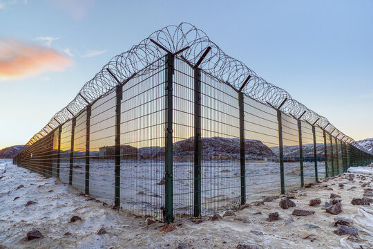 A corner of a fence with barbed wire on the background of the evening sky in an Arctic village.