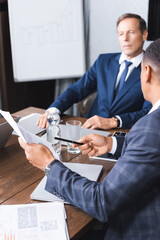 African american businessman pointing with pen at document while sitting near thoughtful executive on blurred background.