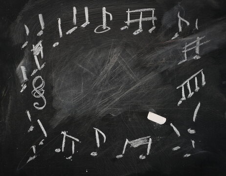 Notes, music symbols, signs frame and border drawn on black chalkboard with white chalk, blackboard background texture
