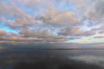 Abstract wide-angle landscape view of tranquil water space. Picturesque cloudy sky reflected in the water. Winter sunset view