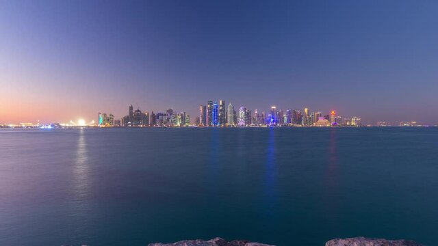 Doha downtown skyline day to night transition timelapse, Qatar, Middle East. Illuminated skyscrapers on a West Bay reflected in a water of Gulf