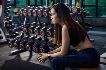 Young woman sitting on a chair at gym after her workout. Female athlete taking rest after exercising at gym.
