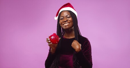 Portrait of smiling African American woman in Santa Claus hat posing isolated over pink background.  New year 2021 holiday concept