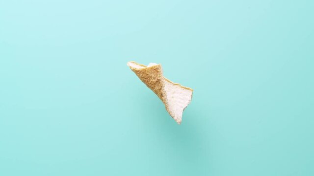 Top view of piece of orange zest rotating on blue cyan background with soft shadow. 4k