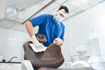 Serious doctor wipes the dentist chair and preparing office