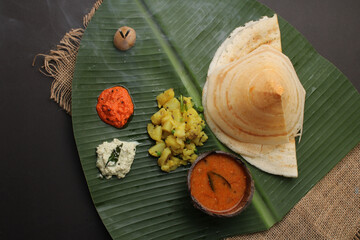 Obraz na płótnie Canvas Paper Masala dosa is a South Indian meal served with sambhar and coconut chutney over fresh banana leaf. 