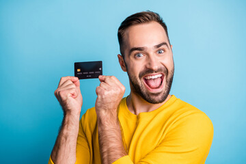 Photo of young handsome excited crazy smiling cheerful man showing credit card isolated on blue color background