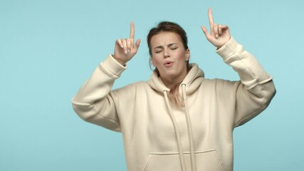 Slow motion of cheerful and carefree blonde girl in white hoodie having fun, dancing and enjoying music, vibing over blue background