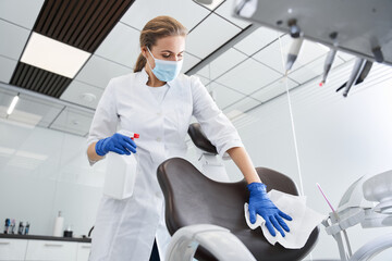 Serious doctor wipes the dentist chair and preparing office