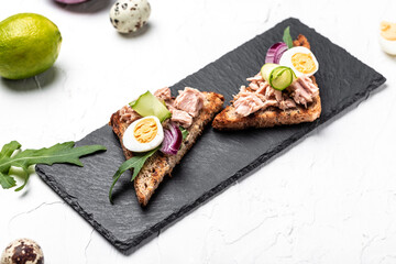 Italian bruschetta sandwiches with canned tuna, cucumber, quail eggs and onions, Toasts with tuna. Delicious breakfast or snack. Top view, flat lay, copy space