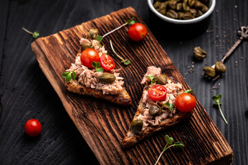 Toasts with tuna. Italian Appetizer bruschetta, sandwiches with canned tuna, tomatoes and capers. delicious healthy food on a dark background, Top view