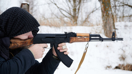 Arab type shooter in a mountainous area against a background of white snow to aim with a Kalashnikov assault rifle