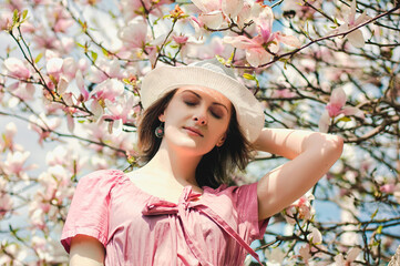 Fototapeta premium Portrait of young attractive woman in spring garden with blooming magnolias. Spring background. Woman's Day. Greeting card. 