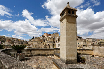 Wide angle landscape of stony Matera city in South of Italy with tower, palm tree in pot and cloudy sky 