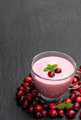 Pink smoothie with cranberry in glass cup on black stone background