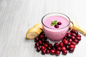 Pink smoothie with cranberry and banana in glass cup on white wooden table