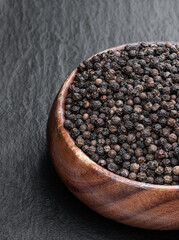Black pepper corn in wooden bowl on black stone background