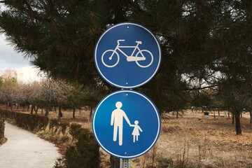 Compulsory footpath and compulsory bicycle path traffic signs together in the beginning of a pathway in a neighborhood with trees and bushes. 