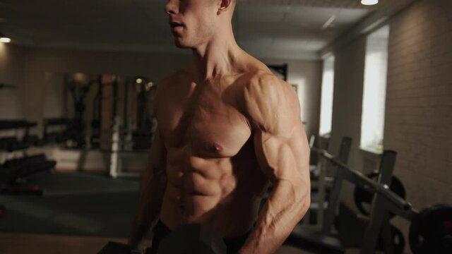 Young muscular man training in the gym and pumping biceps flexing his arms with heavy dumbbells