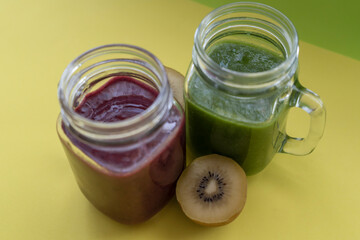 Smoothies with fresh kiwis.Healthy green and red detox drinks in mason jar on yellow background.