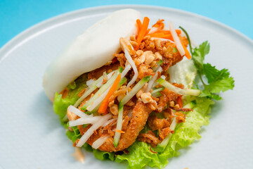 Delicious steamed bao bun on a plate with fried chicken and fresh vegetables - salad, carrots and...