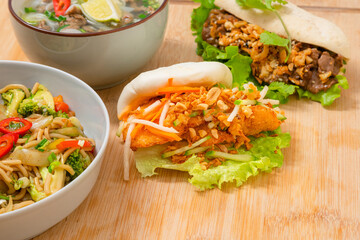 Asian food take away variety on wooden table. Pho soup, bao bun, sea food noodles dishes home delivery