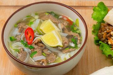 Spicy pho soup bowl with beef meat, lemon slice and chilli peppers on wooden table. Home delivery