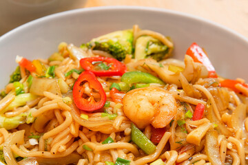 Golden coloured spicy sea food noodles with shrimp, broccoli, chilli pepper in a plate on wooden table