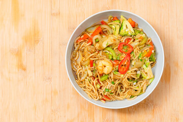 Golden coloured spicy sea food noodles with shrimp, broccoli, chilli pepper in a plate on wooden table