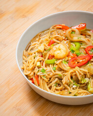 Golden coloured spicy sea food noodles with shrimp, broccoli, chilli pepper in a plate on wooden table