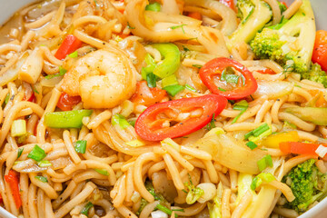 Golden coloured spicy sea food noodles with shrimp, broccoli, chilli pepper in a plate on wooden table