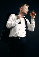 handsome blond man in elegant tuxedo and bow tie posing with glass of whiskey