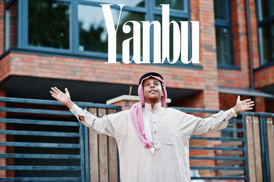 Yanbu - biggest city of Saudi Arabia. Middle Eastern saudi arabian man posed on street against modern building up his hands in the air.