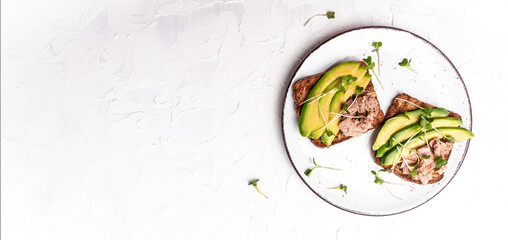 toasts, sandwiches with canned tuna and avocado on a white plate on a light background. Long banner format, top view