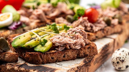 Sandwiches with avocado and tuna fish on wooden cutting board on white background, top view. Healthy breakfast or snack. Food recipe background. Close up